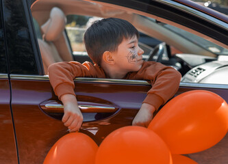 kid boy with orange balloons and spider web on face in car, with head from window or outside from...
