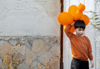 boy kid with orange balloons and spider web drawn on cheek playing outside, left building old door,...