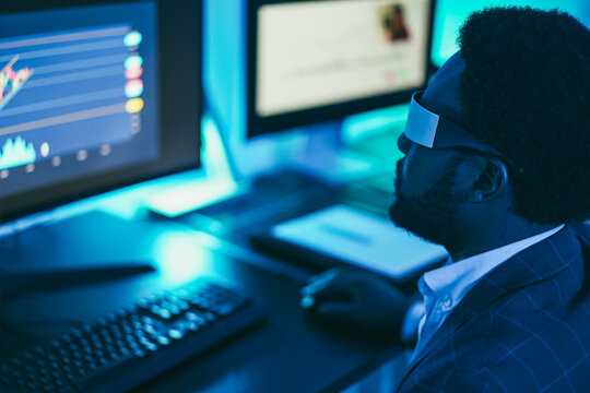 African trader working inside office at night time wearing virtual reality headset - Trading and technology concept - Soft focus on glasses