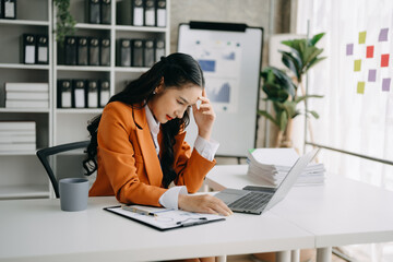 Asian woman feeling migraine head strain.Overworked businesswoman financier while working on laptop and tablet at office.