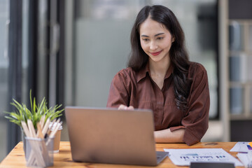 Fototapeta premium Young attractive business asian woman checking searching document her project with laptop computer in the office room.