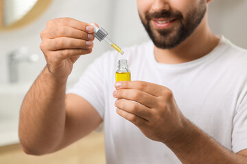 Young man with cosmetic serum in his hands indoors, closeup