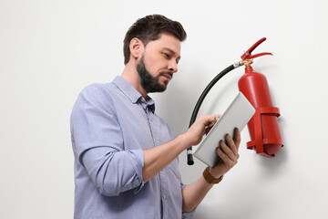 Man with tablet checking fire extinguisher indoors