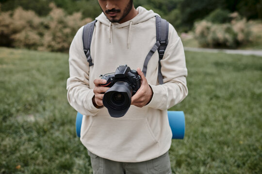 cropped view of indian photographer in hoodie holding professional camera, backpacking and travel