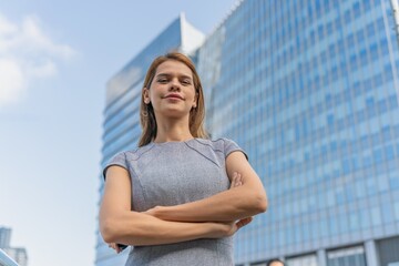 Portrait of a young and successful white caucasian business woman standing in front of a modern cityscape of office buildings