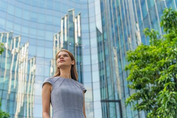 Portrait of a young and successful white caucasian business woman standing in front of a modern cityscape of office buildings