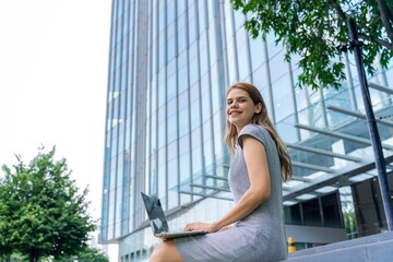 Young caucasian businesswoman working remotely outside her office building 