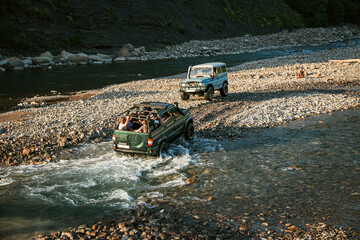 Four-wheel drive cars wade across the river. An off-road trip along the bed of a mountain river. Off-road walking. A jeep ride through the Caucasus Mountains. The concept of active recreation.
