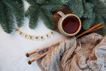 Ceramic cup with tea. Spruce branches on white background. Knitting with needles. Wool scarf is knitted on knitting needles. Concept of New Year's card.Inscription December.