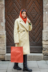 Smiling woman wearing stylish coat in city. Orange knitted scarf. Shopping and seasonal discounts.