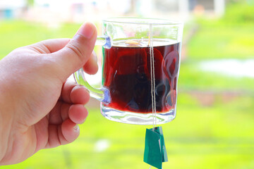 A full cup of hot tea in a man's hand outdoors. Man holding hot tea with a tea bag