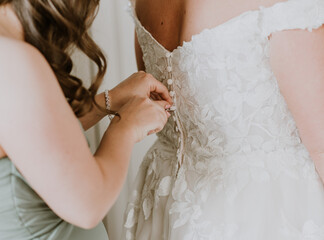 Bridesmaid buttons up the bride into her wedding dress from behind