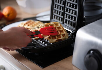 Person prepares waffles on waffle iron at home. Recipe for delicious waffles concept
