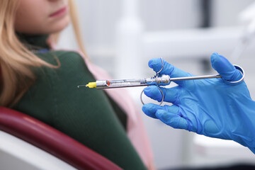 Close up of anesthesia syringe, injector in the hands of a doctor dentist in mask and gloves in...