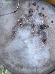 coffee beans being roasted by hand in the traditional way on a wood-fired stove seen from above through the smoke