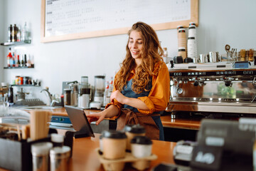 Smiling female barista takes an order from a panchette while standing at the bar counter in a...