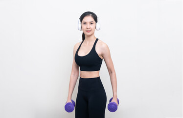 Asian woman wearing black workout clothes with smiling face Exercising with purple dumbbells and cheerful music in headphones against a white or isolated background.