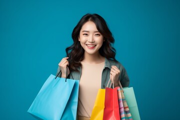 Fototapeta na wymiar Portrait of a happy Asian woman holding shopping bags on blue background