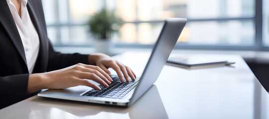 An image featuring a businesswoman's hands as she types on a sleek laptop computer keyboard at a modern office desk - obrazy, fototapety, plakaty