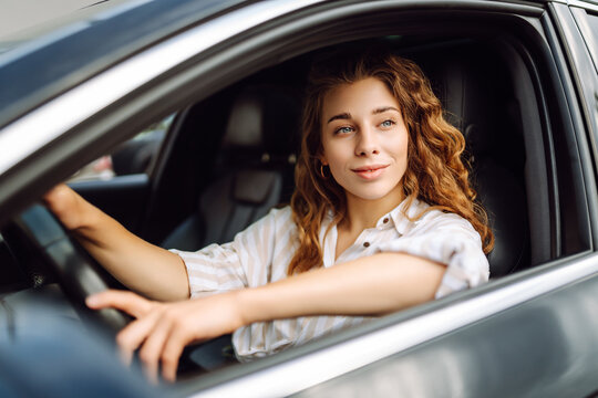 Cute woman in casual clothes is sitting behind the wheel of a car. Traveler-driver. Concept of mode of transportation, travel.