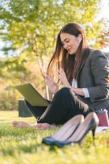 Joyful casual woman with laptop outdoors, sitting on grass with computer, surfing the net or preparing for exams. Technology, education and remote working
