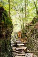 Happy woman in hiking clothes with a yellow backpack walks along a wooden hiking path in the mountains. Hiking, active lifestyle. Outdoor adventure concept.
