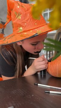 Children are preparing for the Halloween holiday, paint a scary face on a pumpkin with brushes for home decoration, girls decorate a pumpkin for Halloween