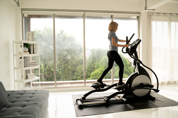 Fit woman using stationary bike for cardio workout at home. Healthy and sporty lifestyle concept - obrazy, fototapety, plakaty