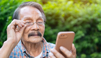 Close up of elder gray beard white hair with glasses looking attention at his smartphone to reading news at garden alone.