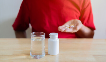Cropped image of senior man in red T-Shirt taking medicine pill at home.
