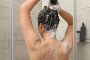 Woman washing hair in shower stall, back view