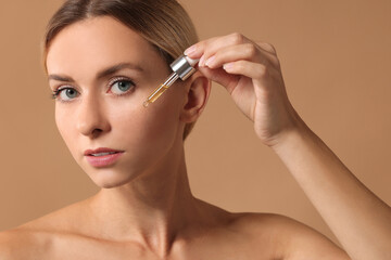 Naklejka premium Beautiful woman applying cosmetic serum onto her face on beige background, closeup