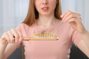 Woman untangling her lost hair from brush indoors, closeup. Alopecia problem