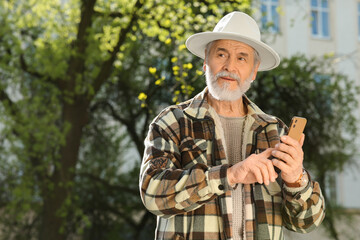 Fototapeta premium Handsome senior man using smartphone outdoors, space for text