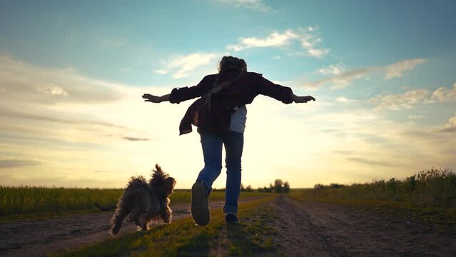 child girl running with a dog in the park. happy family freedom a kid dream concept. silhouette of a child girl running along the road in the park at sunset view from the back with a shaggy sun dog