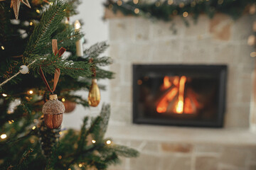 Stylish christmas gold acorn on tree close up against burning fireplace. Beautiful decorated...