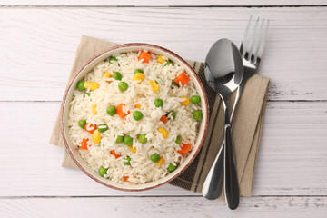Bowl of delicious rice with vegetables served on white wooden table, flat lay
