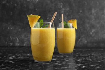 Tasty pineapple smoothie in glasses on black textured table