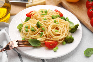 Plate of delicious pasta primavera and ingredients on light gray table, closeup