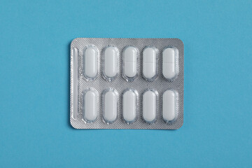 Pills in blister on blue background, top view