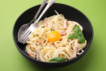 Delicious pasta Carbonara with egg yolk and cutlery on light green background, closeup