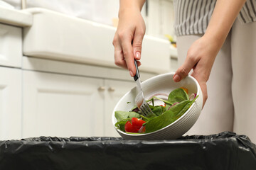Woman throwing vegetable salad into bin indoors, closeup - obrazy, fototapety, plakaty