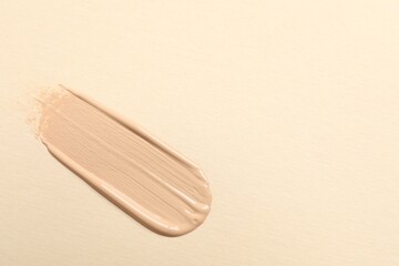 Smear of skin foundation on beige background, top view. Space for text