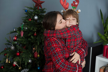 mom and child son in red pajamas hug each other on Christmas morning at home near the Christmas tree