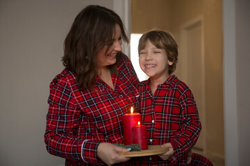 Mom and kid boy in red pajamas hold candle at home on Christmas evening. banner