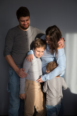 family mom, dad and two children embrace  against a grey background