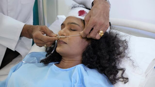 A closeup of a doctor putting in a nasal oxygen tube - medical treatment  patient in coma  breathing problem. A middle-aged female patient recovering from accident - oxygen requirement  respiratory...