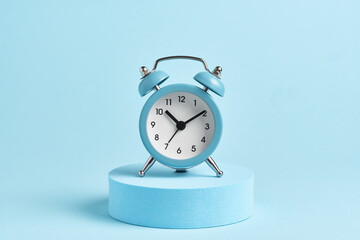 Blue alarm clock on a podium on a blue background.