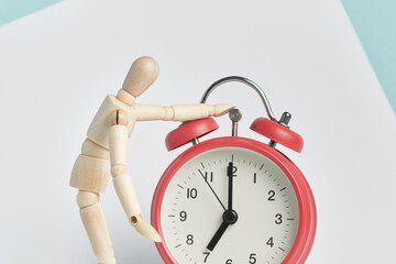 Wooden man stands with his hand on the alarm clock. Waking up in the morning, beginning of the working day.