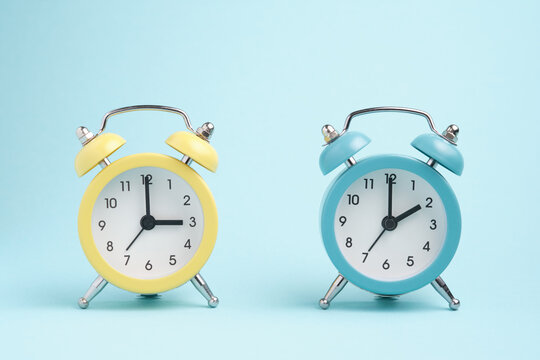 Two alarm clocks of blue and yellow colors, the hands show two o'clock and three o'clock. Concept of winter and summer time.